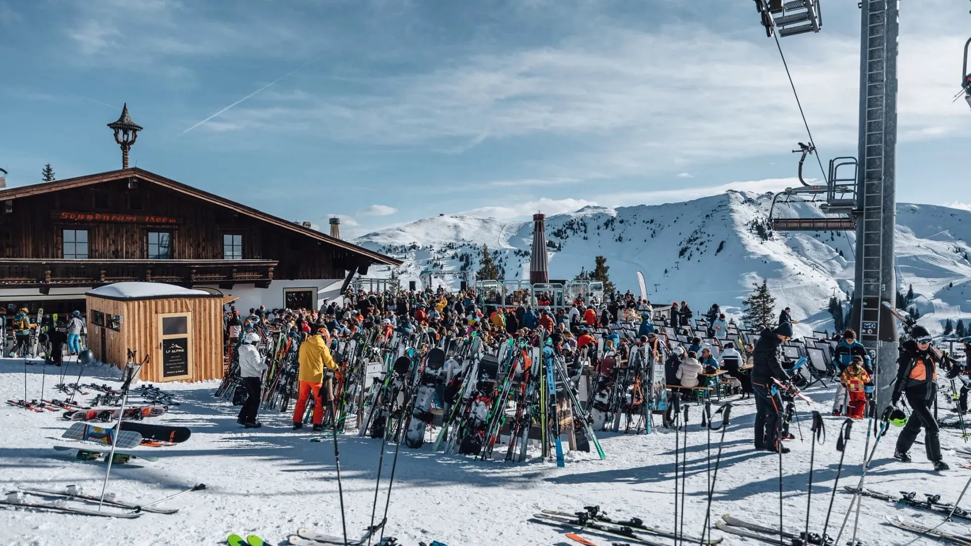 Sonnenrast-Terrasse mit Skiständern und Gästen vor verschneiten Bergen